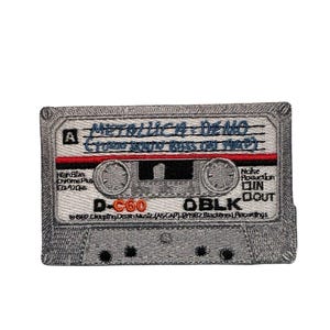 May include: Embroidered patch featuring a gray cassette tape design. The tape has the text "METALLICA DEMO" in blue, with red and black accents. Additional text includes "High Blas Chrome Plus Ea-120us", "D-C60", and "OBLK".