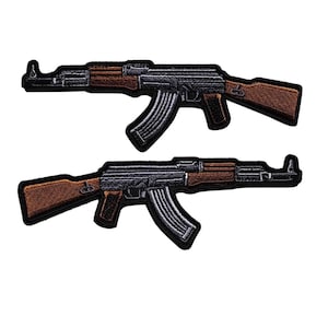 May include: Two embroidered patches featuring an AK-47 rifle design. The patches have a black border, with the rifle body in shades of gray and brown. The magazine is a dark gray color. The patches are likely for clothing or accessories.