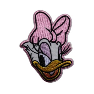 May include: Embroidered patch featuring Daisy Duck's face. The patch has a light pink bow, a gray face, and a yellow beak. The eyes are blue and the mouth is orange. The patch is outlined in a light gray color.