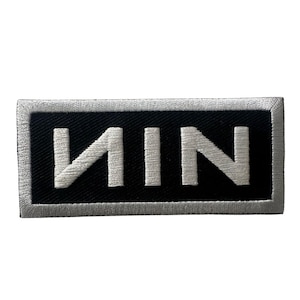 May include: A rectangular patch with the letters "NIN" in white, centered on a black background. The patch has a silver border. The letters are in a bold, sans-serif font.
