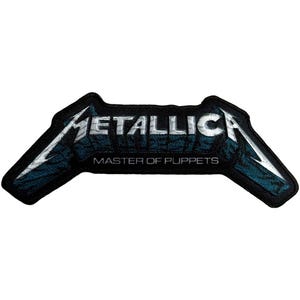 May include: A black and blue embroidered patch featuring the band name "METALLICA" in silver lettering. Below the band name, the text "MASTER OF PUPPETS" is displayed. The patch has a unique, stylized shape.