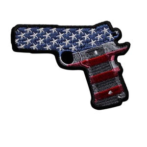 May include: Embroidered patch in the shape of a handgun. The top portion features a blue background with white stars, resembling the American flag. The lower portion has red and gray stripes, with a black border.