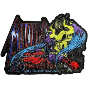 May include: Embroidered patch featuring the word "METALLICA" in blue and white, with a skull and wings design in yellow, purple, and blue. The text "SAN FRANCISCO SYMPHONY" is also included. The patch has a black border.