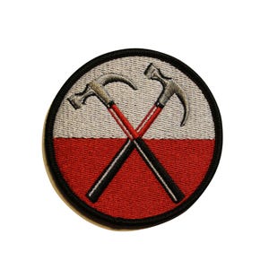 May include: Embroidered patch featuring two crossed hammers on a circular background. The top half is light gray, and the bottom half is red. The hammers are silver with red handles and black shafts, outlined by a black border.