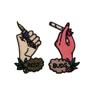 May include: Embroidered patches featuring hands holding a lighter and a joint. The patch on the left says "BEST" and the patch on the right says "BUDS". The patches are surrounded by green leaves and flowers.