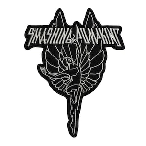 May include: Black and white embroidered patch featuring the text "SMASHING AWAKENING" above a stylized figure with wings. The figure is reaching upwards, holding a flame. The patch has a unique shape with peaks at the top.
