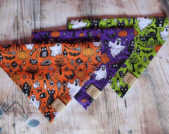 May include: Three Halloween-themed dog bandanas with a black cat, ghost, and pumpkin print. The bandanas are in orange, purple, and green.