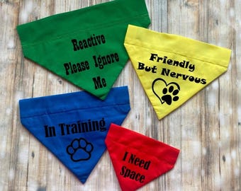 May include: Four triangular pet bandanas in green, yellow, blue, and red. The green bandana reads Reactive Please Ignore Me. The yellow one says Friendly But Nervous with a paw print heart. The blue one says In Training with a paw print. The red one says I Need Space.