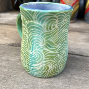 May include: A green ceramic mug with a white wave pattern. The mug has a light blue glaze on the inside.