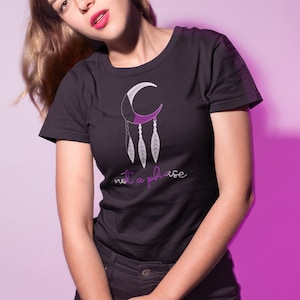 以下が含まれることがあります： 紫と白の三日月と羽根のグラフィックが描かれた黒いTシャツ。グラフィックの下に「not a phase」という文字が紫で印刷されています。
