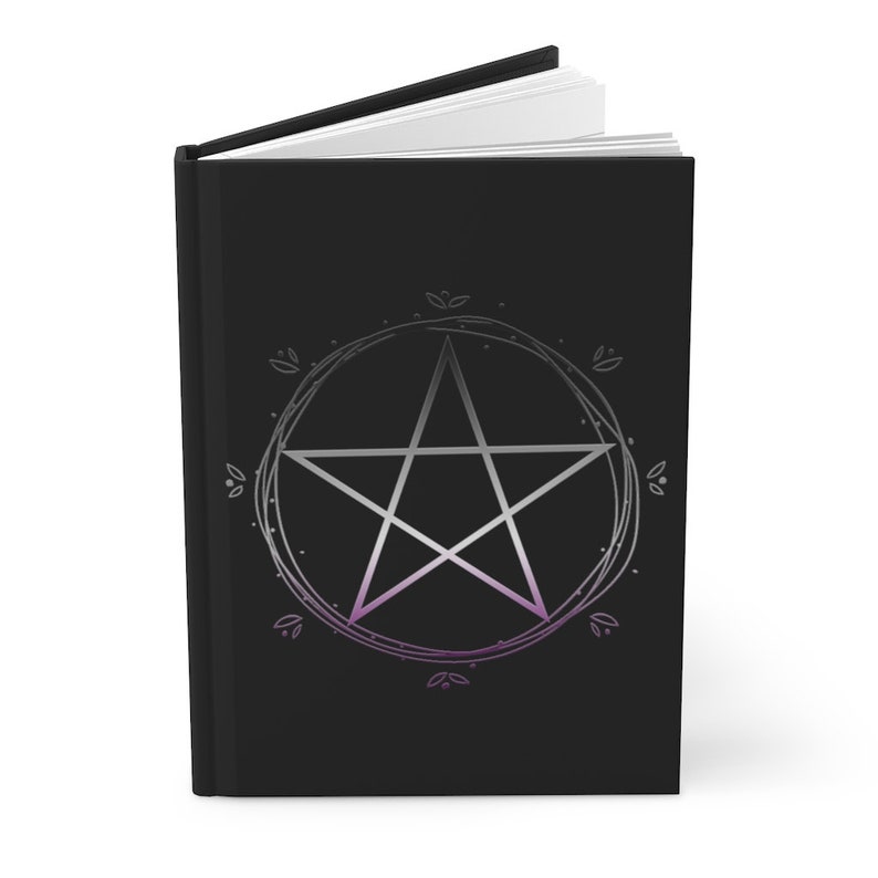 Puede incluir: Un diario negro con un pent&aacute;culo plateado rodeado de un c&iacute;rculo de hojas. El pent&aacute;culo es una estrella de cinco puntas con un degradado de morado y blanco.