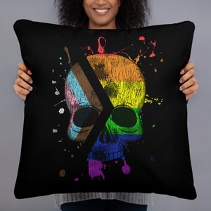 May include: Black throw pillow with a colorful skull design. The skull is split in half, with one side featuring a rainbow flag and the other side featuring a transgender pride flag. The design is surrounded by colorful paint splatters.