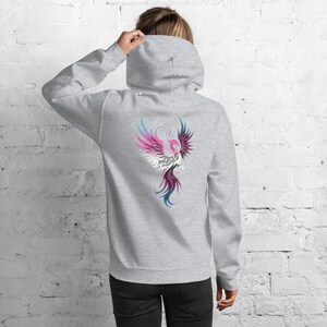 May include: A light gray hoodie with a colorful phoenix design on the back. The phoenix is depicted with pink, white, blue, and purple feathers. The hoodie has a hood and a relaxed fit.