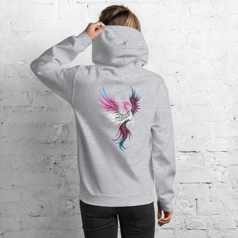 May include: A light gray hoodie with a colorful phoenix design on the back. The phoenix is depicted with pink, white, blue, and purple feathers. The hoodie has a hood and a relaxed fit.