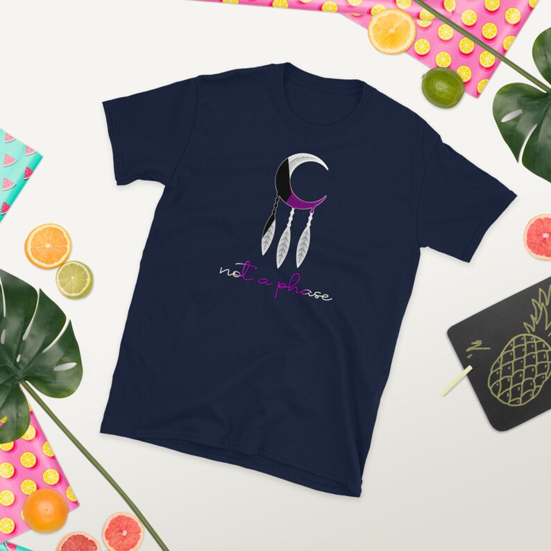 以下が含まれることがあります： 三日月と羽根のデザインが施されたネイビーブルーのTシャツ。デザインの下に「not a phase」という文字が白で印刷されています。