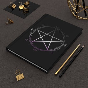 Puede incluir: Un cuaderno negro con un pentagrama plateado dentro de un c&iacute;rculo con un degradado morado. El cuaderno est&aacute; sobre una superficie gris texturizada con dos l&aacute;pices y clips de papel dorados.