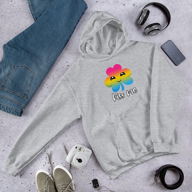 Pu&ograve; includere: Una felpa con cappuccio grigia con un design a trifoglio arcobaleno e il testo "Kiss Me".