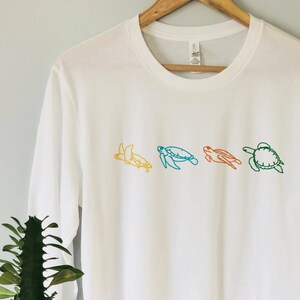 May include: A white long-sleeved t-shirt with a line of four colorful sea turtles embroidered on the front.