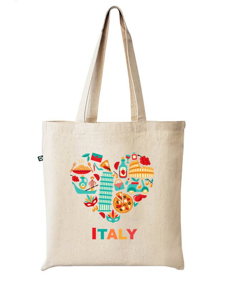 Op de afbeelding: Beige canvas draagtas met een kleurrijk hartvormig ontwerp met Italiaanse iconen, waaronder pasta, pizza en de scheve toren van Pisa. Het woord "ITALY" is gedrukt in rood, oranje en geel. De tas heeft lange hengsels.