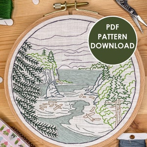 May include: A completed embroidery hoop featuring a nature scene of a lake, trees, and a rocky shore. The hoop is on a wooden surface with embroidery floss and scissors. The text "PDF PATTERN DOWNLOAD" is on a green circle.