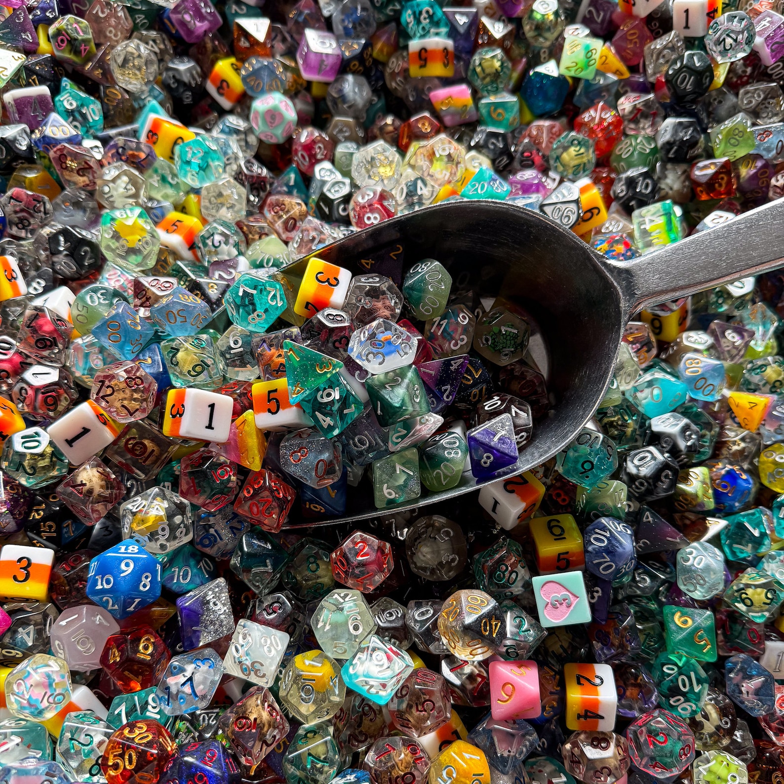 Silver metal scoop half submerged in a pile of different brightly colored DnD dice.