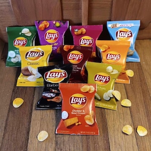 May include: A collection of Lay's potato chip bags in various flavors, including Classic, Cheddar & Sour Cream, and Barbecue. The bags are brightly colored and arranged on a wooden surface, with scattered chips.