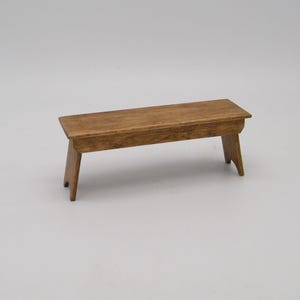 May include: A small, wooden bench with a rectangular seat and angled legs. The bench is stained a warm brown color, showcasing the wood grain. This miniature furniture piece is ideal for dollhouses or craft projects.