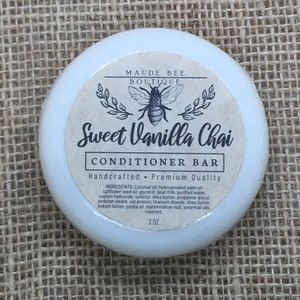 以下が含まれることがあります： ミツバチのロゴと「MAUDE BEE BOUTIQUE」と「Handcrafted - Premium Quality」のテキストが書かれた、白い丸いSweet Vanilla Chaiコンディショナーバー。バーは3オンスです。