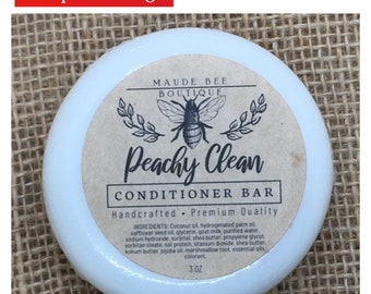 May include: A white round container with a brown label that reads "MAUDE BEE BOUTIQUE Peachy Clean CONDITIONER BAR Handcrafted Premium Quality INGREDIENTS: Coconut oil, hydrogenated palm oil, safflower seed oil, glycerin, goat milk, purified water, sodium hydroxide, sorbitol, shea butter, propylene glycol, sorbitan oleate, oat protein, titanium dioxide, shea butter, kokum butter, jojoba oil, marshmallow root, essential oils, colorant. 3 OZ"