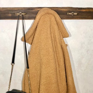 May include: A brown faux fur hooded jacket hanging on a wooden coat rack with a black leather crossbody bag with a gold chain strap.