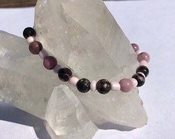 May include: A bracelet made with pink, black, and white beads. The bracelet is on a white crystal rock.