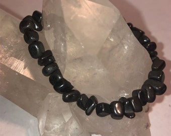 May include: Black gemstone bracelet made of small, irregular shaped beads. The bracelet is displayed on a white crystal.