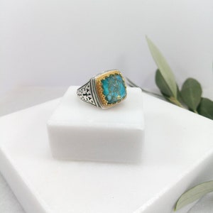 May include: A silver ring with a turquoise stone set in a gold bezel. The ring has a detailed design on the band.