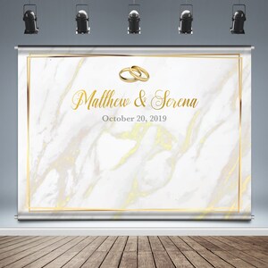 May include: White marble backdrop with a gold frame and gold rings. The text "Matthew & Serena" and "October 20, 2019" is printed in gold.