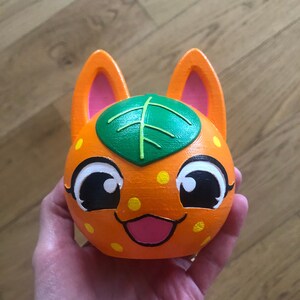 May include: Orange and green cartoon character with large eyes, a leaf on its head, and a pink tongue sticking out.