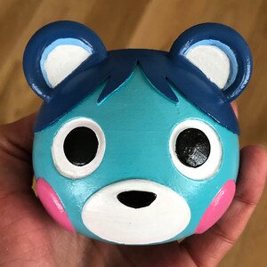 May include: A blue and white ceramic figurine of a bear with pink cheeks. The bear has large, black eyes and a white nose.