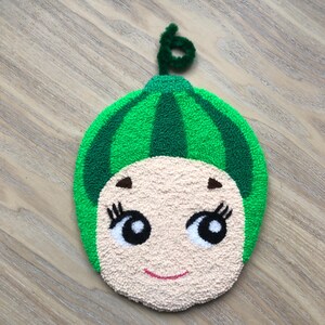 Puede incluir: Un juguete de peluche con forma de sand&iacute;a verde con una cara sonriente, ojos negros y pesta&ntilde;as. El juguete tiene un tallo verde en la parte superior.