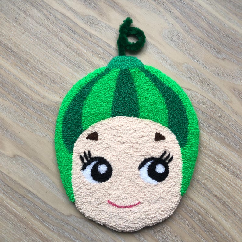 Puede incluir: Un juguete de peluche con forma de sand&iacute;a verde con una cara sonriente, ojos negros y pesta&ntilde;as. El juguete tiene un tallo verde en la parte superior.