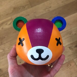 May include: A purple, orange, and white ceramic planter shaped like a bear with a cute face. The planter has green and blue accents on the ears.