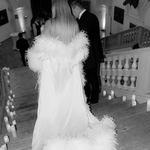 May include: A person wearing a white feather trimmed gown walking down a set of stairs with candles lining the steps.