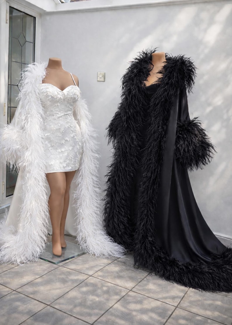 Puede incluir: Dos batas largas hasta el suelo con mangas largas y ribete de plumas en los bordes. Una bata es blanca y se combina con un minivestido blanco con escote coraz&oacute;n y detalles de encaje floral. La otra bata es negra y de aspecto satinado.