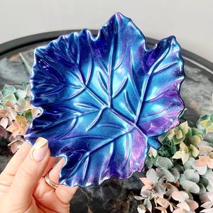 May include: A blue and purple iridescent leaf-shaped dish. The dish is made of resin and has a glossy finish.