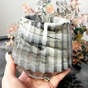 May include: A grey and white marbled ceramic planter with a fluted design. The planter has a wide, round opening and a narrow base.