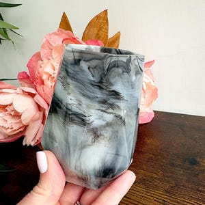 May include: A faceted tumbler featuring a marbled pattern of swirling black, grey, and white tones. The vessel has a geometric, multi-sided shape with a smooth, glossy finish, creating a distinct visual contrast between the dark and light colours.