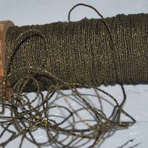 May include: A wooden spool of metallic gold-colored thread. The thread is tightly wound around the spool, with loose strands spilling out. The spool's wooden ends are visible, adding a rustic touch to the craft supply.
