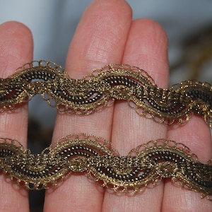 Puede incluir: Primer plano de dos tiras de adorno decorativo. El adorno tiene un diseño ondulado con una combinación de colores dorados y marrón oscuro. El adorno tiene un borde festoneado y una textura tejida.