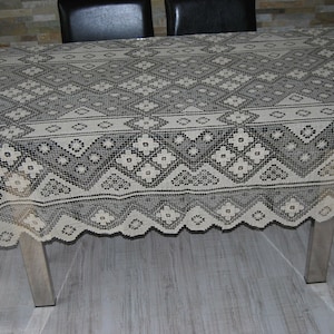 May include: A white crocheted tablecloth with a black geometric pattern. The tablecloth is draped over a table with a wooden top and metal legs.