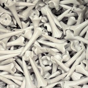 May include: A close-up shot of a pile of white golf tees. The tees have a flower-shaped top and a long, pointed stem. The tees are made of a smooth, glossy material.