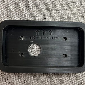 May include: Black plastic plate with three arrows pointing upwards and the text "The Space Leg". The plate has a round hole in the center and three smaller holes around the edge.