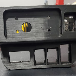 May include: Black plastic panel with multiple rectangular cutouts and a round hole. The panel has a textured surface.